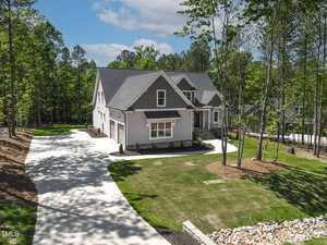 Located at 3923 Cedar Knolls Drive in Youngsville, this two-story gray house with white trim sits on a spacious lot with a well-maintained lawn, surrounded by trees. A long driveway leads to the attached garage under a partly cloudy sky.
