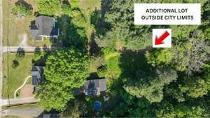 Aerial view of several houses surrounded by trees, with a grassy lot marked by a red arrow and labeled "Additional Lot Outside City Limits" in a white box at the top right of the image.