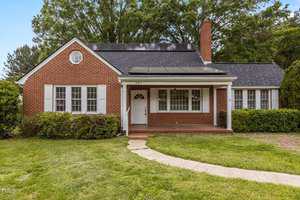 A single-story brick house with white shutters at 801 Williamsboro Street, Oxford, featuring a covered front porch, solar panels on the roof, a chimney, and a well-kept lawn with a curved walkway leading to the front door.