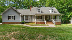 A gray, single-story house with white trim and a brick foundation at 450 S Stratford Drive, Henderson. The covered front porch overlooks a grassy yard with a curved concrete walkway, surrounded by trees in the background.