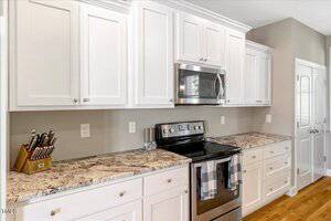 A modern kitchen with white cabinets, marble countertops, stainless steel electric stove and microwave, a knife block, and two gray-striped towels hanging on the oven handle.