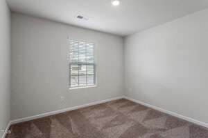 Empty room with beige carpet, white walls, a single window with blinds, and a ceiling light. Sunlight is coming through the window, and there are electrical outlets on the walls.