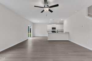 Unfurnished open-plan living area with light-colored walls and wood-look flooring, a ceiling fan, recessed lighting, and a kitchen with white cabinets and granite countertops. Sliding doors lead to the outside.