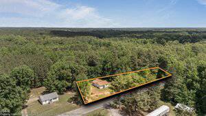 Aerial view of 3899 Warrenton Road, Henderson: house and yard outlined with orange lines to indicate property boundaries, surrounded by dense forest, neighboring houses, and a road in front.