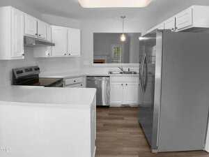 Modern kitchen with white cabinets, stainless steel appliances, electric stove, double sink, and wood-style flooring. A pendant light hangs over the sink area, and there is a pass-through window to another room.