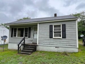 A small, single-story gray house on 246 Keene Street in Henderson features black shutters, a covered front porch with steps, weathered siding, and patchy grass in the yard beneath an overcast sky.