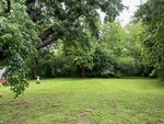 A grassy yard at 106 Summitt Avenue, Oxford is bordered by dense green trees under a cloudy sky. On the left side of the lawn, a tree stump and a small pedestal or birdbath are visible.