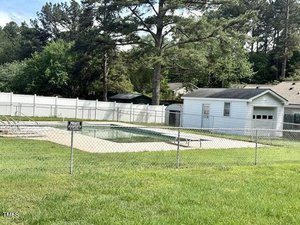 A fenced-in rectangular swimming pool with metal steps is next to a small white building. There is a sign that reads "Private Property." Trees and additional buildings are visible in the background.