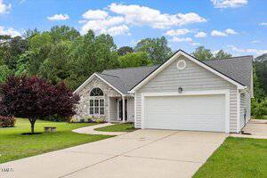 Charming single-story house in Creedmoor featuring gray siding, stone accent around the front window, dark roof shingles, two-car garage, wide driveway, and a green lawn with trees and shrubs at 1969 Bowles Avenue.