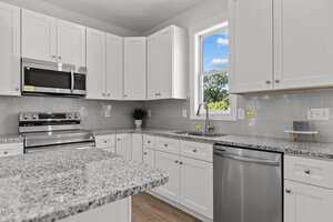 A modern kitchen with white cabinets, stainless steel appliances, gray subway tile backsplash, granite countertops, and a window above the sink letting in natural light.