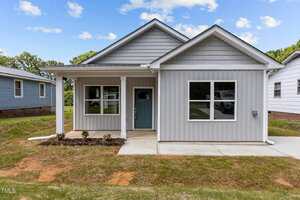 A single-story, gray house with white trim at 815 Goshen Street in Oxford features a covered front porch, blue front door, and three visible windows. The front yard has a small flower bed and patchy grass, with neighboring houses on either side.