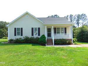 A charming single-story house at 3803 Ridgewood Drive in Franklinton features white siding, black shutters, a covered front porch with white railings, steps from the walkway, and a spacious green lawn with trees in the background.
