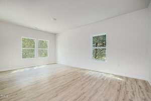 Empty room with light-colored wood flooring, white walls, and three windows letting in natural light. No furniture or decorations are present.