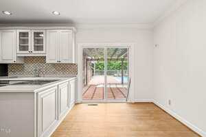 A bright kitchen and dining area with light wood flooring, white cabinets, and glass sliding doors leading to a covered patio and pool outside.
