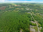 Aerial view of a rural area near 15 US Highway in Stovall, with dense forest, open fields, and scattered houses. Roads wind through farmland and patches of trees visible in the distance under a partly cloudy sky.