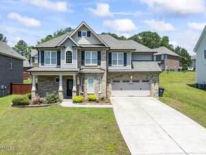 Two-story suburban house at 1499 Fireside Lane in Creedmoor with brick and siding exterior, attached two-car garage, and driveway. The front yard features grass, shrubs, and a landscaped area. Neighboring homes are visible in the background.