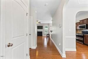 A hallway with hardwood floors leads to a living area featuring a fireplace and wall-mounted TV. To the right, there is a kitchen with dark wood cabinets and stainless steel appliances.