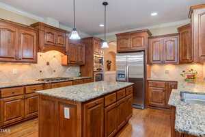 Spacious kitchen with wooden cabinets, granite countertops, a central island, stainless steel appliances, hardwood floors, and pendant lighting above the island.