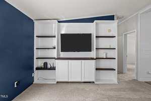A built-in white entertainment center with dark wood shelves holds a flat-screen TV, a modem, a router, and a small speaker. The walls are painted navy blue and white, and the floor is carpeted in beige.
