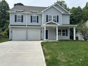 This two-story house at 431 Mayview Drive in Creedmoor features light gray siding, blue shutters, a covered front porch, and a double garage. It sits on a slightly sloped lot with a concrete driveway and patchy green grass out front.