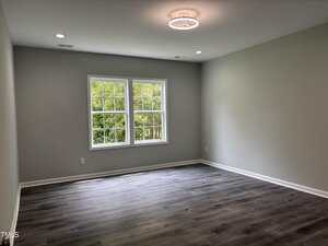 Empty room with light gray walls, a ceiling light, two windows with white trim, and dark wood-style flooring. Room appears clean and well-lit with natural light coming in from the windows.
