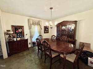A formal dining room with a wooden dining table, eight matching chairs, a large china cabinet, a sideboard, framed art, a window with drapes, and a chandelier hanging from the ceiling.