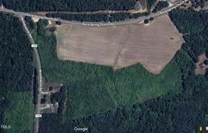 Aerial view of a rural area near 000 Rock Spring Church Road in Henderson, featuring a large open field bordered by woods. Rock Spring Church Road and Woodcreek Drive intersect near the top, with a few buildings and driveways visible nearby.