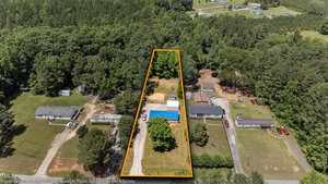 Aerial view of a rectangular property at 3157 Gela Road, Oxford, outlined in orange, featuring a house, driveway, trees, and open yard amid other houses, wooded areas, and picturesque rural landscape.