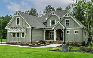 A modern, single-family house at 3913 Cedar Knolls in Youngsville features gray siding, white trim, and a gabled roof on a well-manicured lawn with shrubs and a stone path, surrounded by trees under a partly cloudy sky.