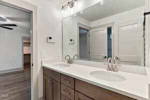 A modern bathroom with a double sink vanity, wood cabinets, silver faucets, a large mirror, two towel holders, and a view of an adjacent room and closet through open doors.