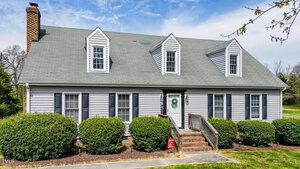 A gray two-story house with white trim, black shutters, and dormer windows at 110 W Quail Ridge Road, Oxford. Features include a brick chimney, central ramp and steps to the front door, and neatly trimmed bushes lining the front.