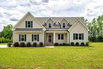 A newly built light-colored house at 1779 Walter Grissom Road in Kittrell features three dormer windows, a front porch, and neatly trimmed bushes, set on a large grassy lawn with trees in the background under a partly cloudy sky.