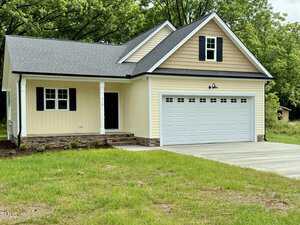 A single-story yellow house with white trim at 512 Hicksmill Road, Oxford, features a covered front porch, double garage with white doors, stone accents near the foundation, and a concrete driveway surrounded by grass and trees.