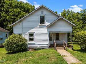 A white, single-story wooden house with a front porch and ramp sits on a grassy lawn at 312 W Front Street, Oxford, surrounded by green trees and bushes under a blue sky.