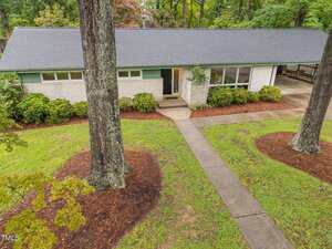 A single-story house at 402 Forest Road in Oxford features a dark gray roof, white brick exterior, and large windows. It sits behind a paved walkway, surrounded by trees and well-maintained landscaping with mulch and green grass.