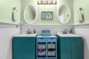 A bathroom with two teal vanities, white sinks, and round mirrors on a light green wall. Between them is a blue storage unit with baskets. Decorative items and towels are neatly arranged.