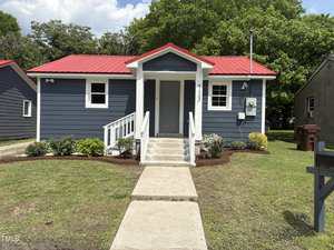 A small single-story house at 713 Champion Street in Henderson, featuring blue siding, a red metal roof, and white trim. The front entrance has double doors, steps, a short walkway, and is surrounded by a neatly maintained lawn.