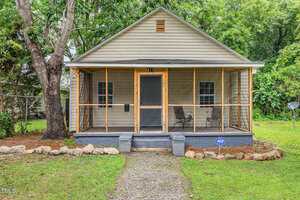 A small beige house at 611 Rowland Street, Henderson, features a screened front porch with two chairs and a dark front door. A stone path leads to the steps, an ADT security sign is by the porch, and trees and greenery surround the home.