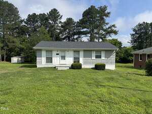 Charming single-story gray house at 124 Kearney Avenue, Oxford, featuring a dark roof, two front windows, a small front porch with steps, and two trimmed bushes on a spacious grassy lawn with trees and another home in the background.
