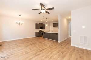 A spacious open-plan living area features light wood flooring, white walls, a ceiling fan, and a chandelier. The modern kitchen has dark wood cabinets, stainless steel appliances, and pendant lights over an island.