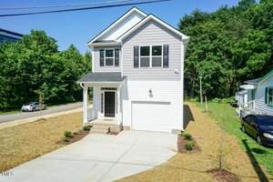 Contemporary two-story home at 213 Clement Avenue, Oxford, with light gray siding, white trim, a black door, covered front porch, single-car garage, concrete driveway, and minimal landscaping amidst mature trees and greenery.