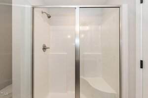 A modern shower with white walls, a built-in bench on the right, a glass sliding door, and a metal showerhead with matching handle on the left.