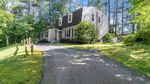 A two-story house with gray siding and white trim sits at 3070 Cameron Drive in Henderson, beside a paved driveway, surrounded by grass, trees, and shrubs under a clear sky.