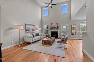 A modern living room with light gray walls, hardwood floors, a white sofa, two armchairs, a wooden coffee table, a fireplace, floor lamp, and large windows allowing natural light into the space.