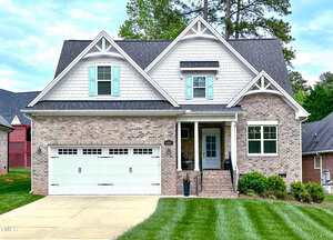A two-story suburban house at 409 Eagle Court with a light brick exterior, white trim, gray shingles, teal window shutters, a covered front porch, and double garage. The green lawn blends into the inviting Henderson neighborhood.