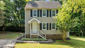 Located at 113 Fox Run in Henderson, this two-story beige house with dark shutters and a brick foundation features a covered front porch, white railing, concrete driveway, and a well-kept lawn with trees and shrubs.