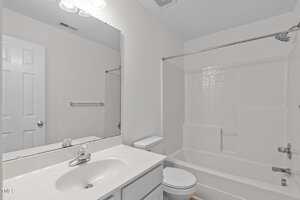 A clean, white bathroom with a sink, a toilet, a large mirror, and a bathtub with a showerhead and a curtain rod. The walls and tiles are white, and lighting is provided by overhead fixtures.