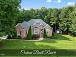 A large brick ranch-style house at 517 Belmont Circle, Wake Forest, with a manicured lawn, bushes, and trees surrounding the property. The home features multiple gables and white-trimmed windows. "Custom Built Ranch" text is overlaid at the bottom.