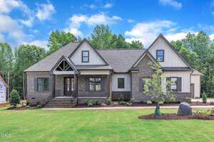 A newly built, single-story suburban house at 3920 Cedar Knolls Drive, Youngsville features dark brick and white siding exterior, gable roofs, front steps, young landscaping, and a large grassy lawn on a clear, sunny day.