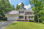 Charming two-story house in Creedmoor with light-colored siding, red shutters, an attached double garage, and a covered front porch with columns on 2750 Michelle Court. Sloped lawn is surrounded by trees under a partly cloudy sky.